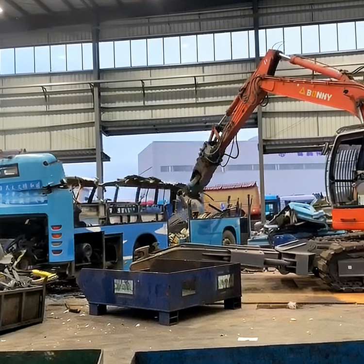 Car dismantling shear dismantling a scrap bus inside a recycling workshop