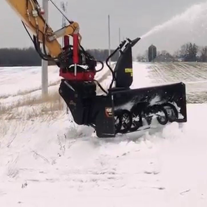 loader-mounted snow blower attachment clearing snow in an open field