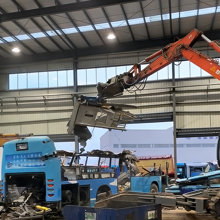 Vehicle dismantling shear lifting a bus section in an indoor dismantling plant