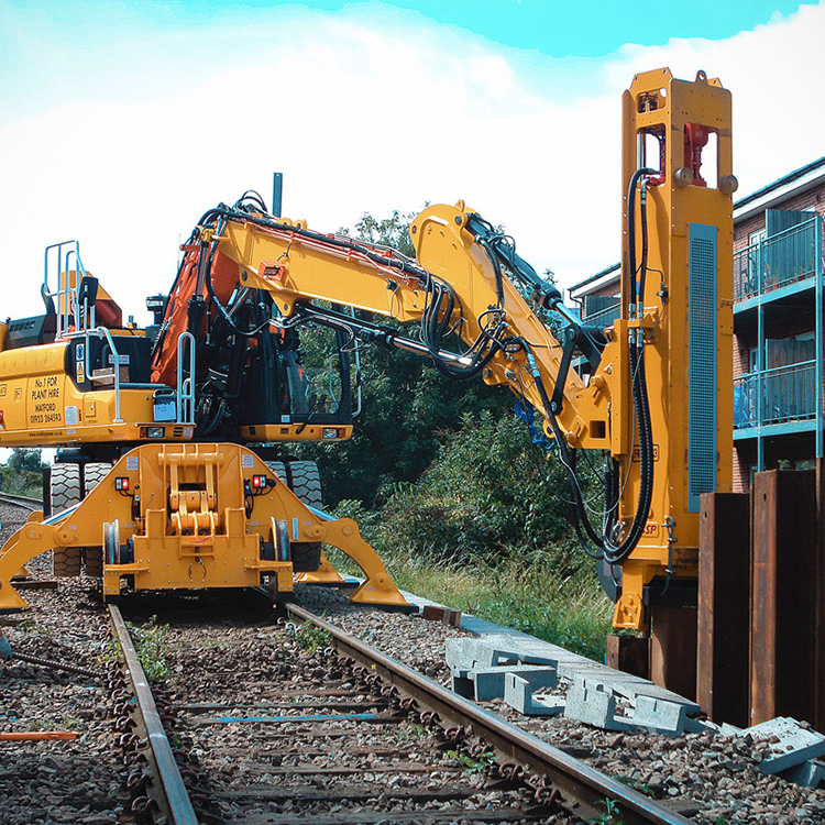 Excavator mounted vibratory pile driver on rail construction site