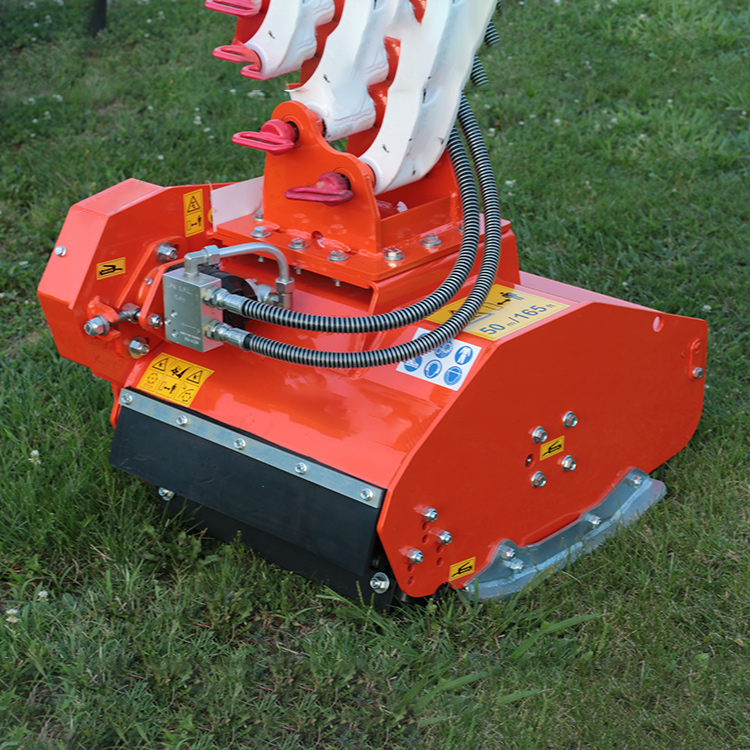 Mini excavator brush mower attachment positioned over grass in field application